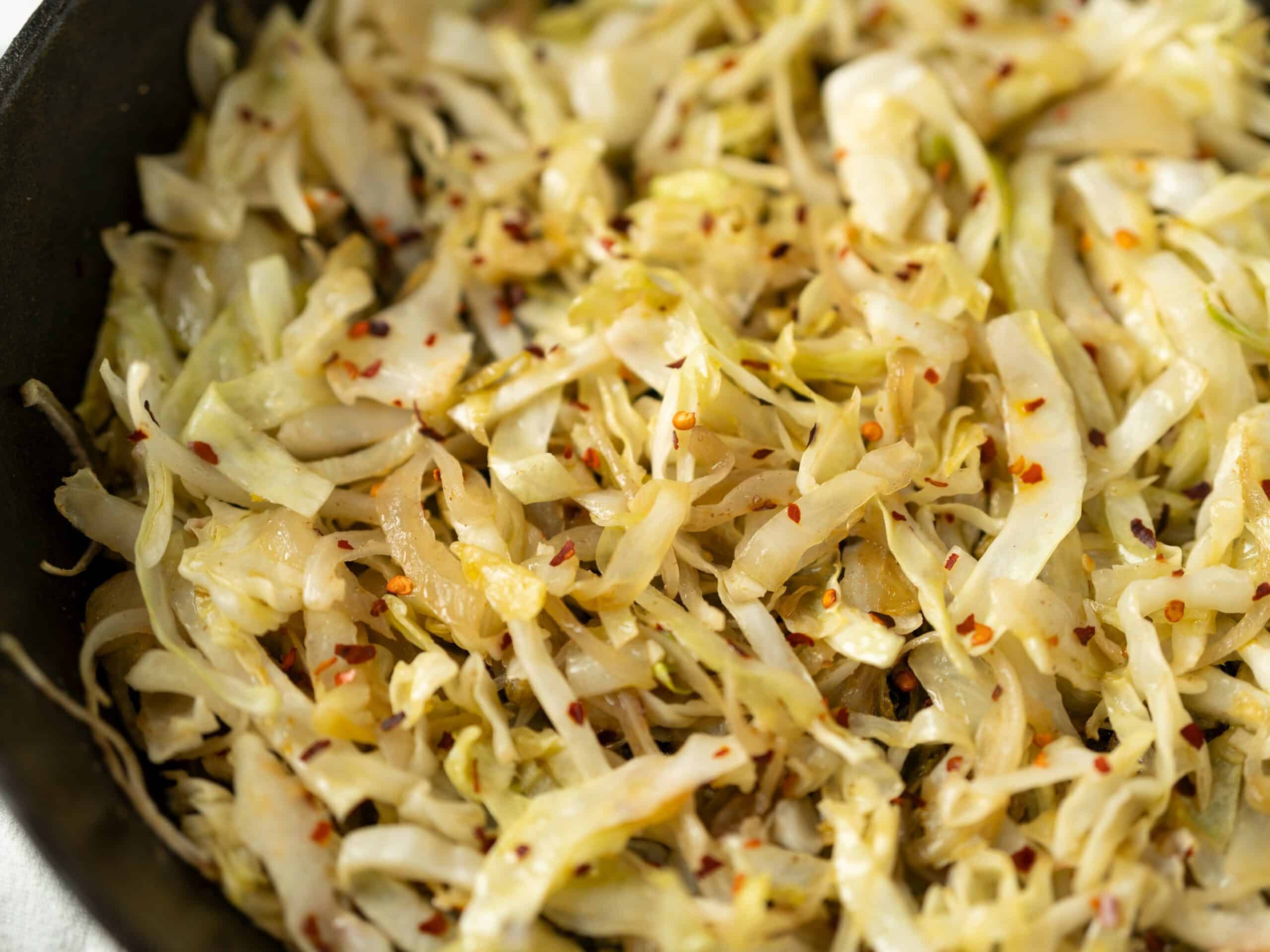 Sautéed shredded cabbage with red pepper flakes, garlic, and spices in a skillet, showcasing a flavorful and easy side dish or healthy recipe from Hey Recipe.