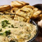 Creamy spinach and cheese dip served in a skillet with grilled garlic bread and mushrooms, perfect for appetizer or party snacks, fresh and flavorful.