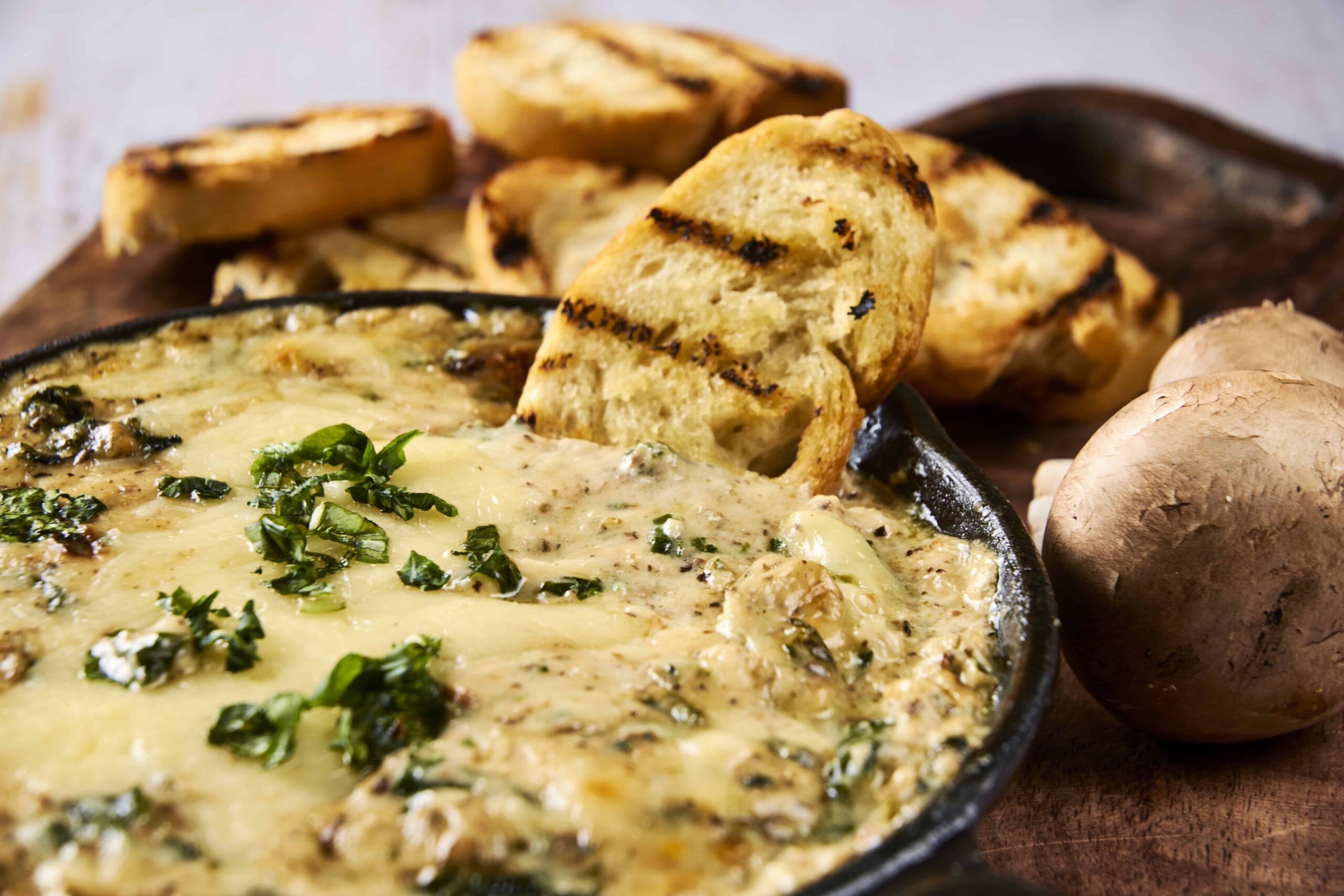 Creamy spinach and cheese dip served in a skillet with grilled garlic bread and mushrooms, perfect for appetizer or party snacks, fresh and flavorful.