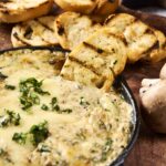 Creamy mushroom and cheese dip served with grilled bread slices and fresh mushrooms on a rustic wooden board. Perfect appetizer for gatherings and cozy meals.