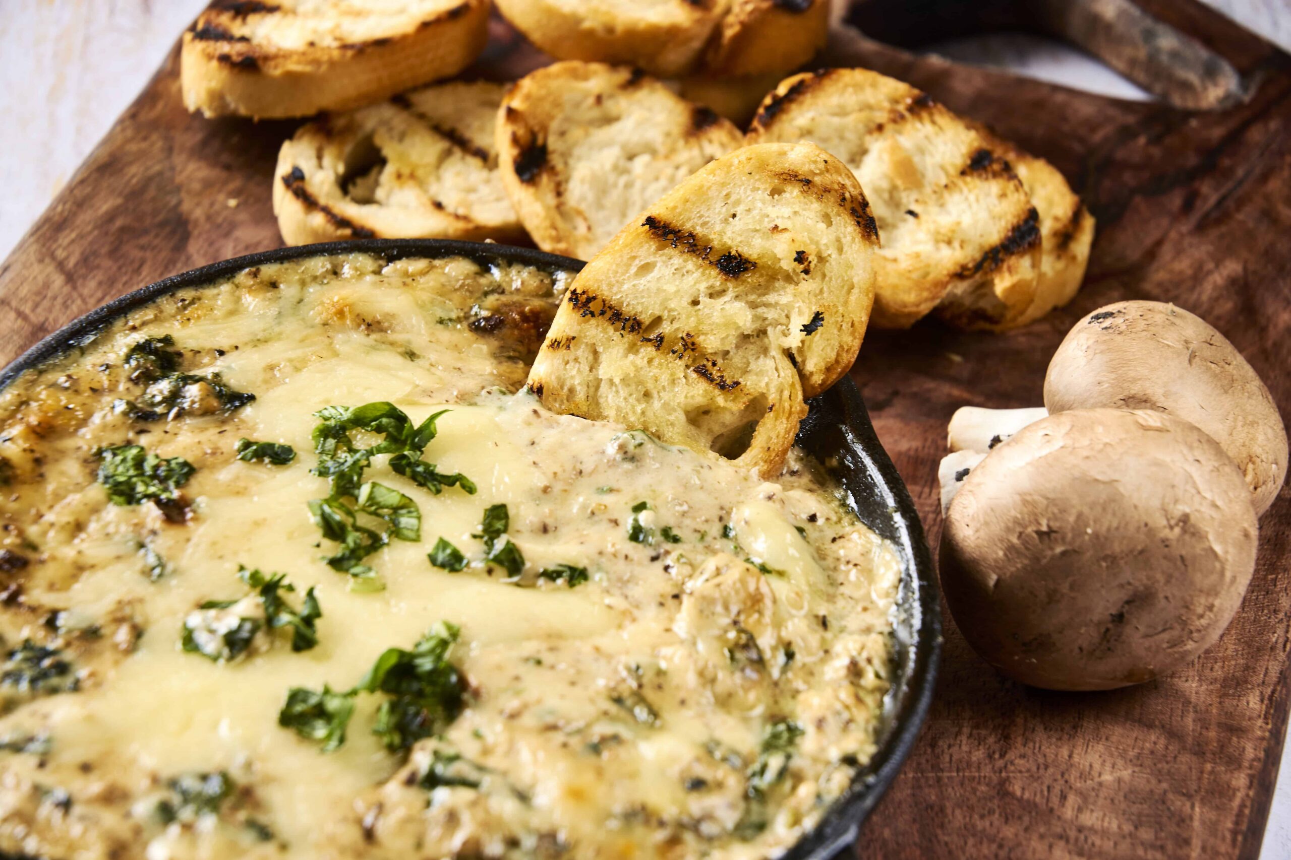 Creamy mushroom and cheese dip served with grilled bread slices and fresh mushrooms on a rustic wooden board. Perfect appetizer for gatherings and cozy meals.