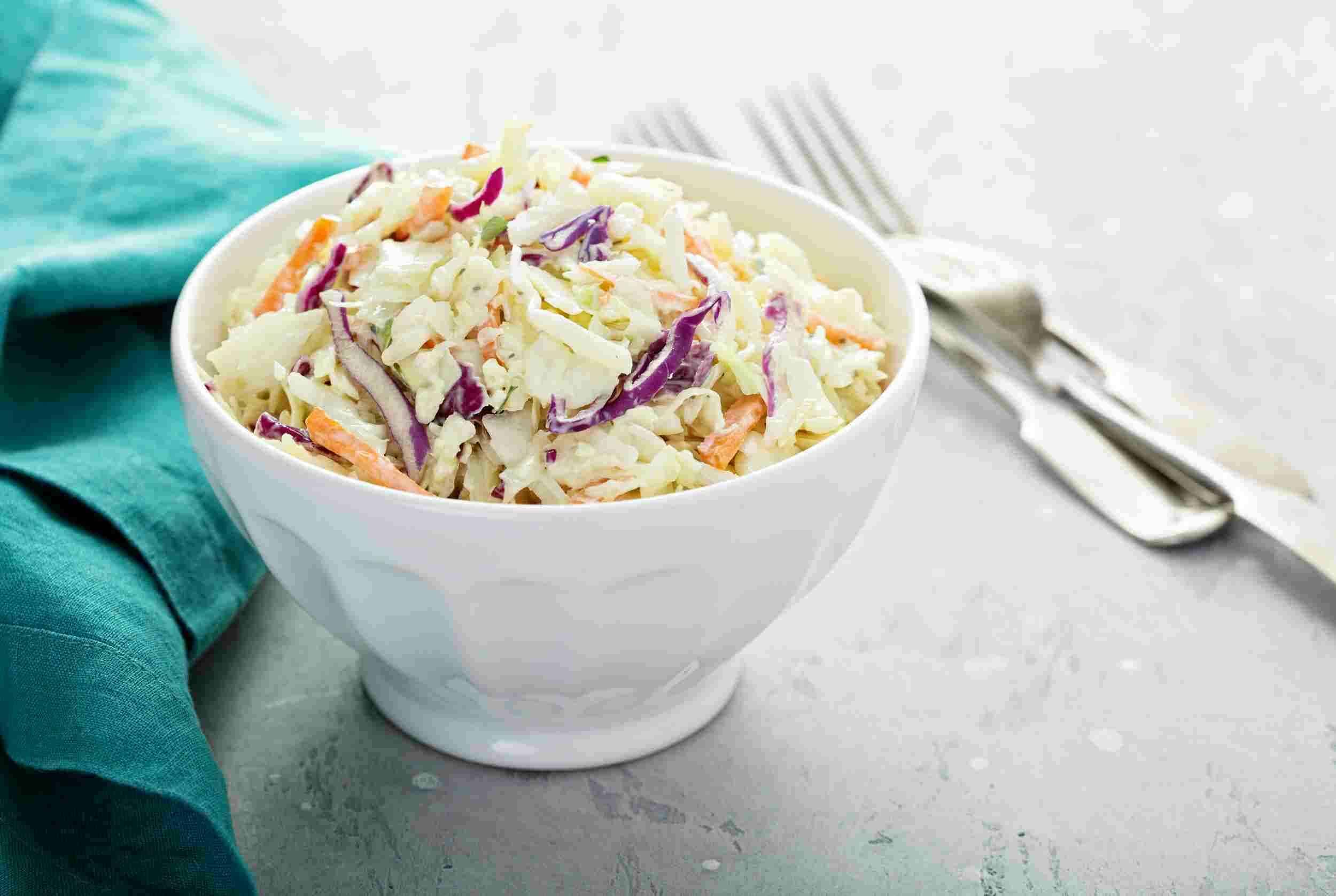 Creamy coleslaw salad with shredded cabbage, carrots, and purple cabbage in a white ceramic bowl. Perfect for summer picnics and barbecues, this easy homemade coleslaw recipe is fresh and flavorful.