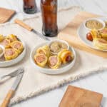 Savory sausage & cheese puff pastry bites served with mustard dipping sauce on white plates, garnished with wooden serving boards and neutral table setting for appetizer or party snack.