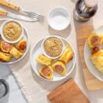 Air fryer sausage rolls with mustard sauce on white plates, served on wooden boards, with condiments and cutlery, ready for a tasty snack or appetizer.