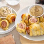 Flavored sausage wrapped in crispy pastry served with mustard sauce on a white plate.
