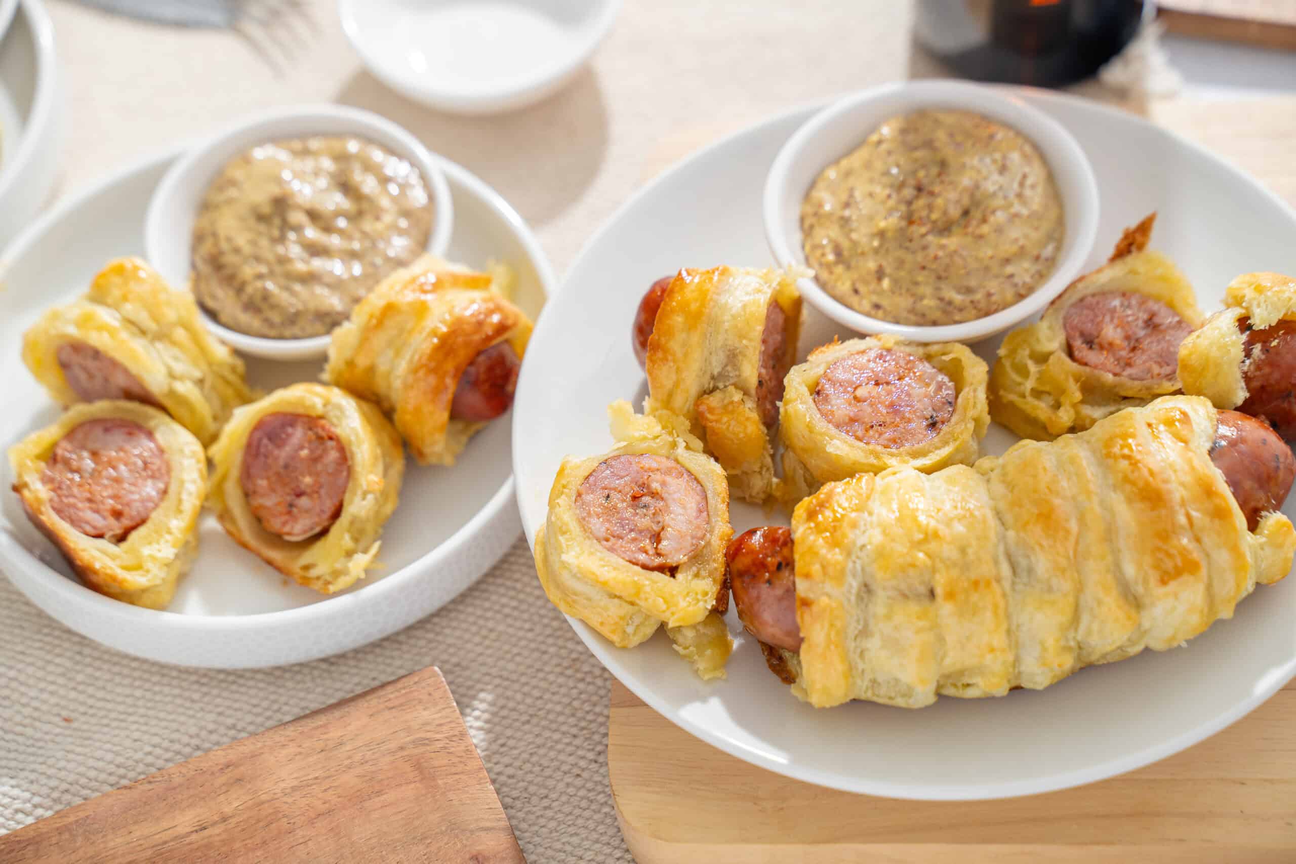 Flavored sausage wrapped in crispy pastry served with mustard sauce on a white plate.