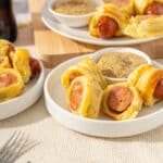 Golden fried sausage rolls served with mustard dipping sauce and mustard seeds on the side, perfect for quick snacks or parties.