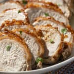 Juicy roasted pork tenderloin sliced and garnished with fresh herbs on a white serving platter. Perfect for a delicious meal, featuring tender meat with crispy edges.