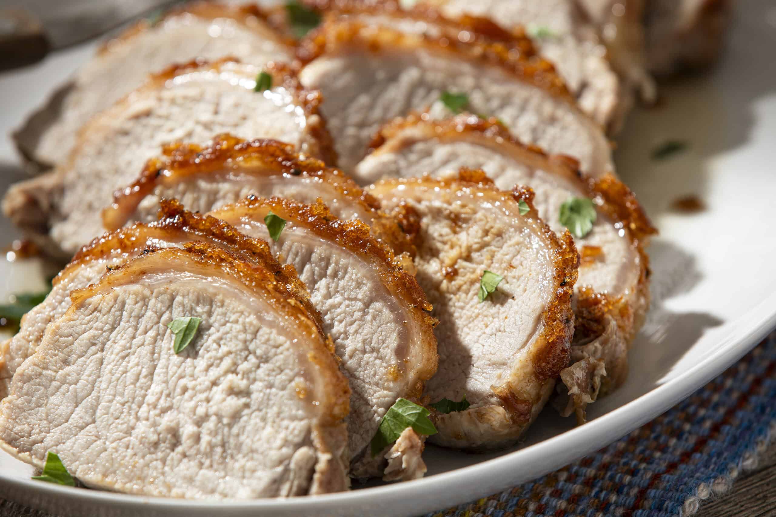 Juicy roasted pork tenderloin sliced and garnished with fresh herbs on a white serving platter. Perfect for a delicious meal, featuring tender meat with crispy edges.
