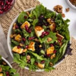 Fresh kale and mixed greens salad with feta cheese, pomegranate seeds, and walnuts, served in a white bowl for a healthy, colorful meal.