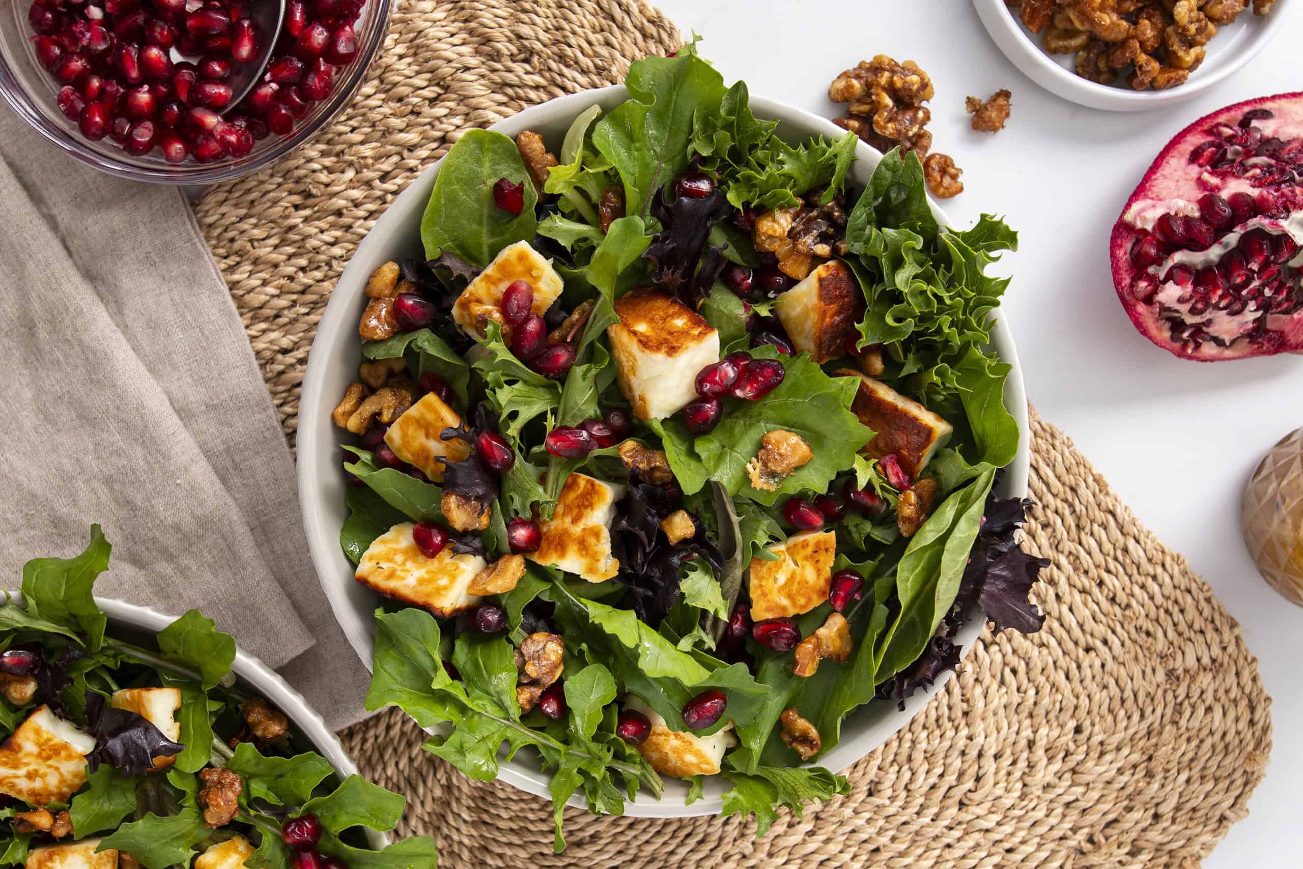 Fresh kale and mixed greens salad with feta cheese, pomegranate seeds, and walnuts, served in a white bowl for a healthy, colorful meal.