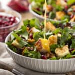 Fresh pomegranate and goat cheese salad with mixed greens, walnuts, and honey vinaigrette on a white bowl, perfect for healthy eating and nutritious meal ideas.