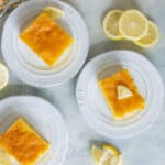 Lemon bars with a golden, crunchy crust and tangy lemon topping served on white plates with fresh lemon slices around. Perfect for summer desserts or afternoon tea.