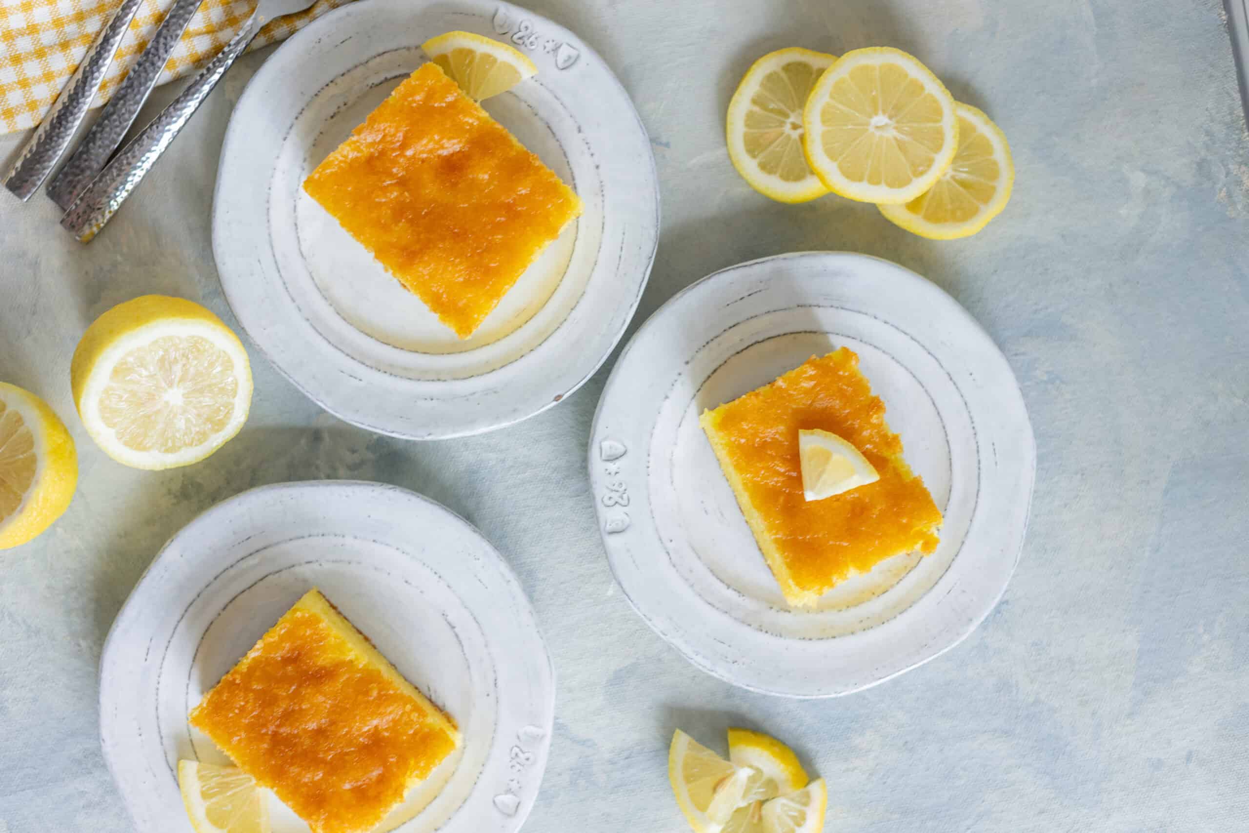 Lemon bars with a golden, crunchy crust and tangy lemon topping served on white plates with fresh lemon slices around. Perfect for summer desserts or afternoon tea.