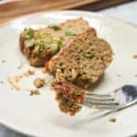 Ground meat loaf with herbs served on a white plate, close-up image showing the moist and seasoned texture of the meatball loaf, ideal for comfort food recipes and delicious main courses.