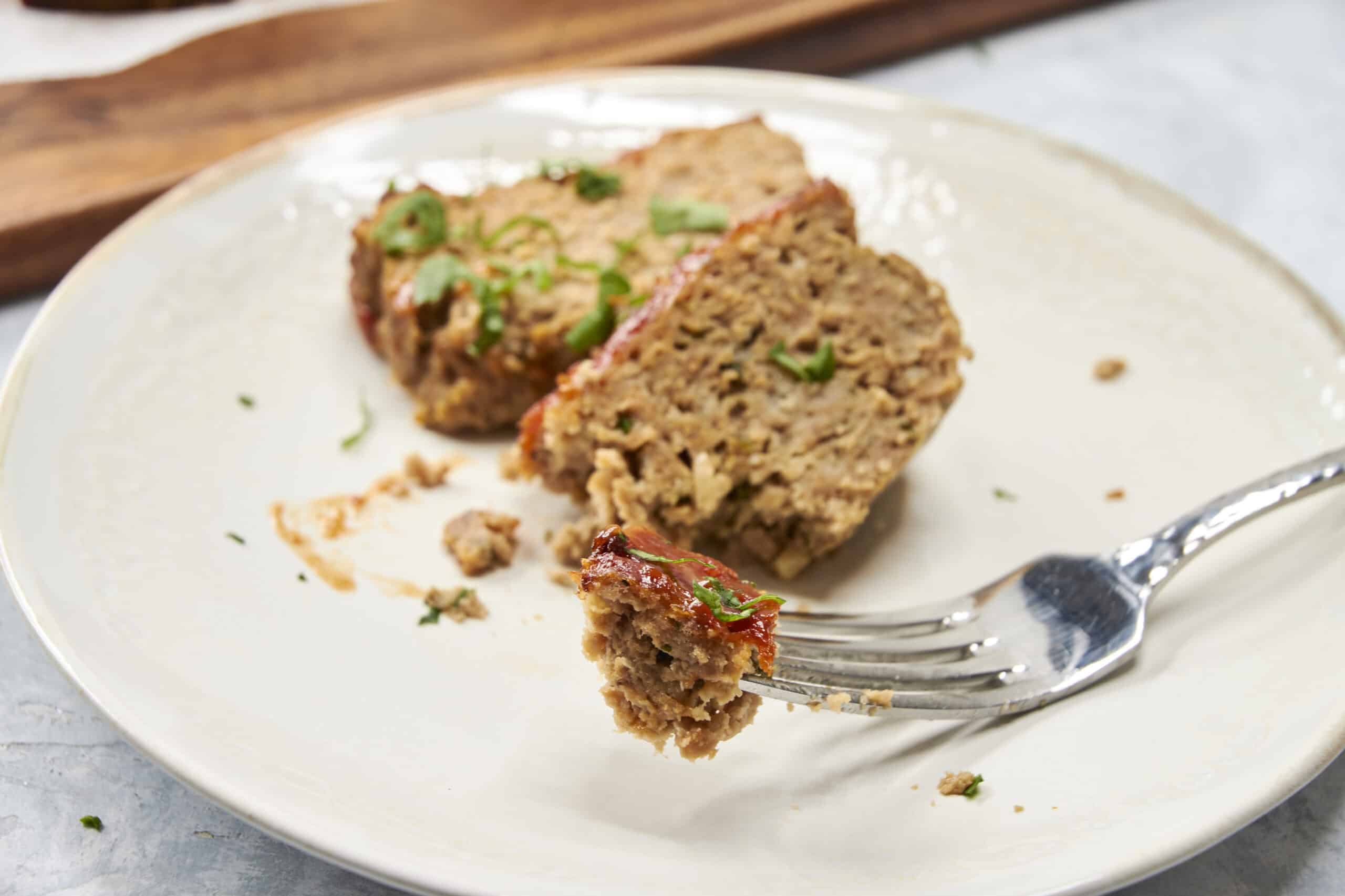 Ground meat loaf with herbs served on a white plate, close-up image showing the moist and seasoned texture of the meatball loaf, ideal for comfort food recipes and delicious main courses.