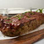 Juicy meatloaf topped with tomato sauce, garnished with fresh herbs on a wooden serving board. Perfect comfort food recipe, easy to make, with flavorful ingredients for family dinner.