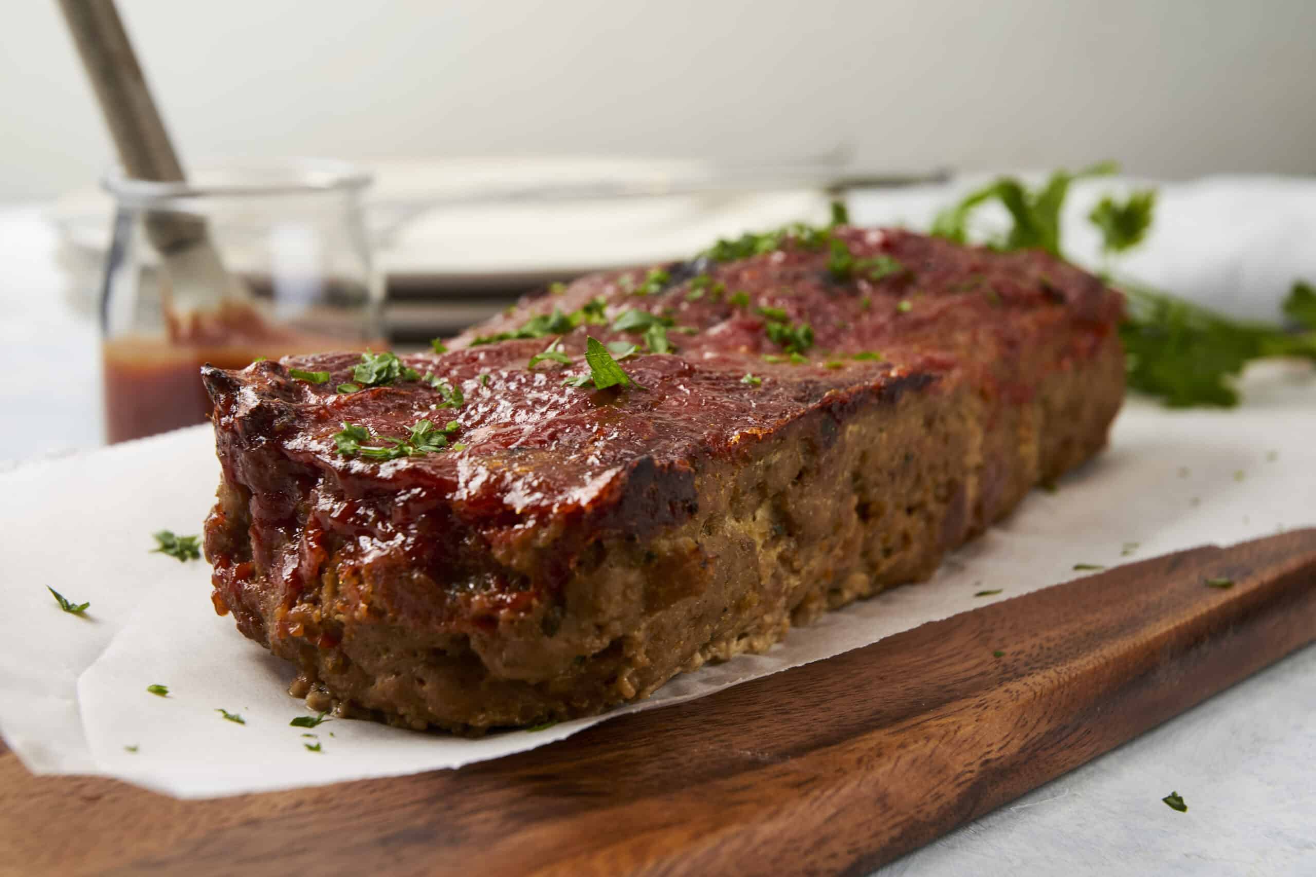 Juicy meatloaf topped with tomato sauce, garnished with fresh herbs on a wooden serving board. Perfect comfort food recipe, easy to make, with flavorful ingredients for family dinner.