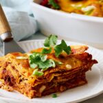 Layered Mexican lasagna with crispy tortillas, savory chili, melted cheese, and fresh herbs on a white plate. Perfect for a hearty, flavorful Mexican-inspired dinner.