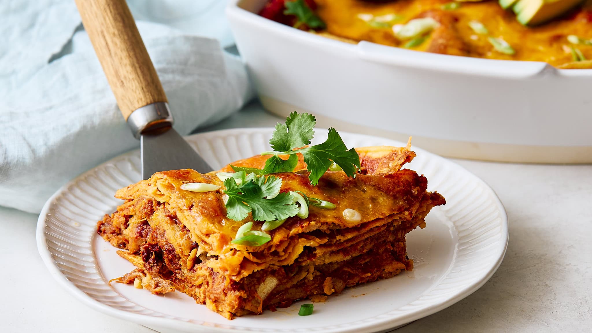 Layered Mexican lasagna with crispy tortillas, savory chili, melted cheese, and fresh herbs on a white plate. Perfect for a hearty, flavorful Mexican-inspired dinner.