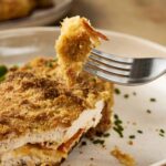 Crispy breaded chicken cordon bleu with green beans on a white plate.