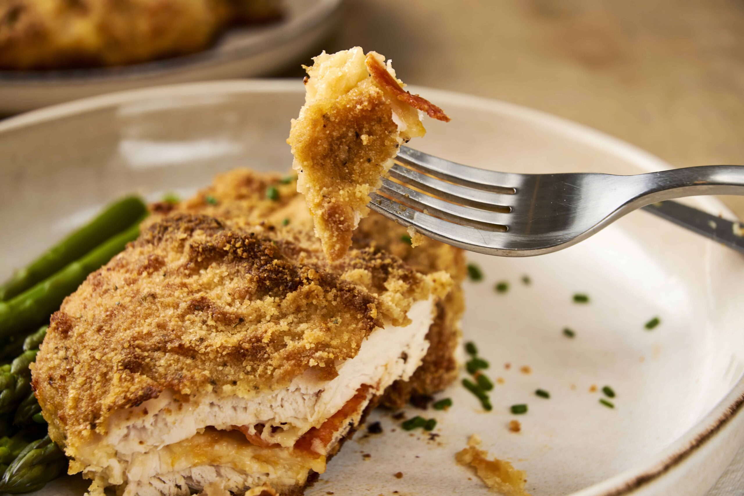 Crispy breaded chicken cordon bleu with green beans on a white plate.