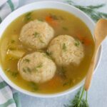 Fluffy homemade chicken meatballs in savory broth garnished with fresh dill, served in a white bowl with a wooden spoon, perfect for comforting soups and easy dinner recipes.