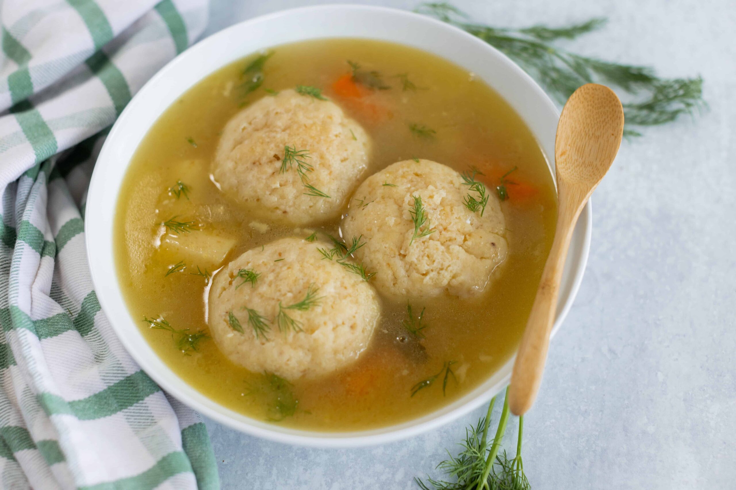 Fluffy homemade chicken meatballs in savory broth garnished with fresh dill, served in a white bowl with a wooden spoon, perfect for comforting soups and easy dinner recipes.