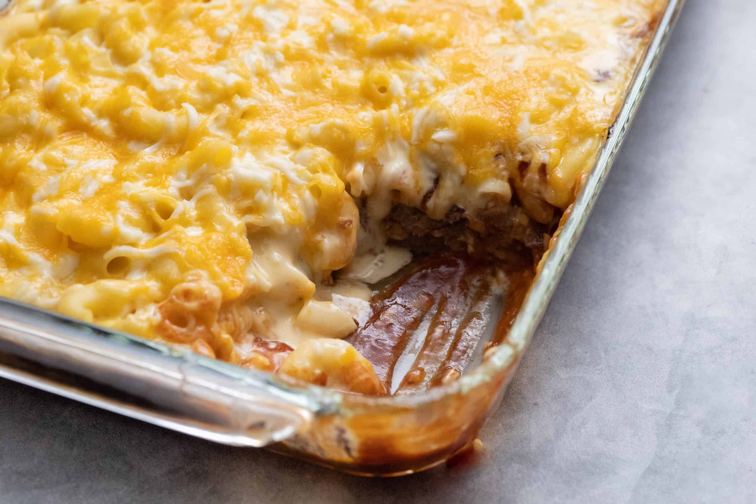 Creamy baked macaroni and cheese casserole topped with melted cheddar cheese in a glass dish. Perfect comfort food with a golden, cheesy crust.