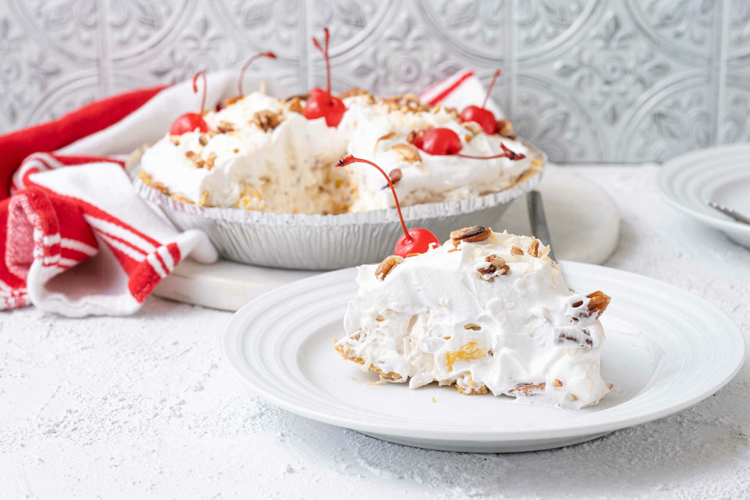 Creamy cherry and pecan dessert on a white plate with a larger serving dish in the background, garnished with fresh cherries and nuts, perfect for a holiday or special occasion.