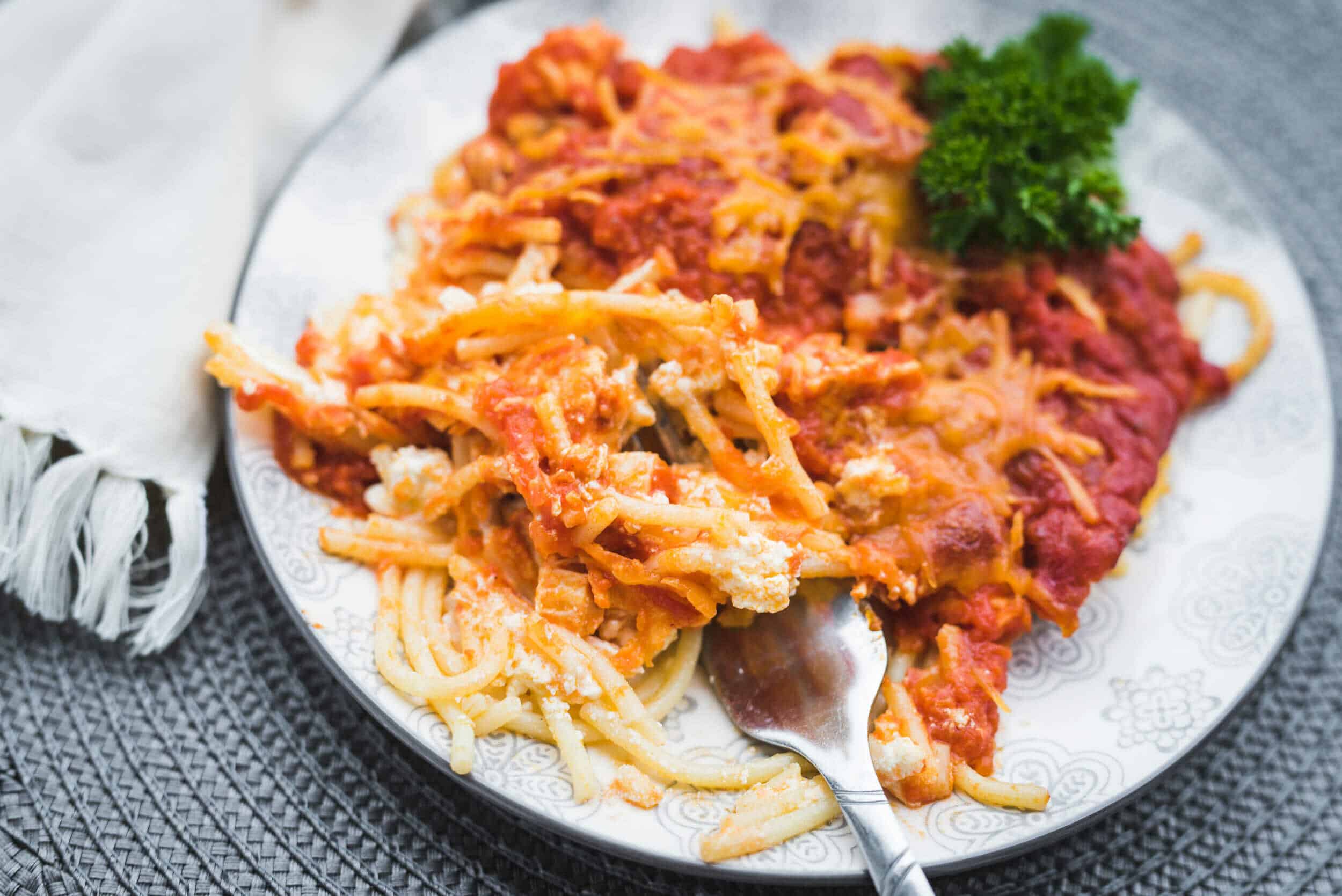 Creamy spaghetti with tomato sauce and melted cheese served with fresh parsley garnish on a decorative plate.