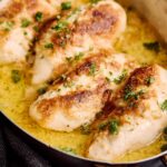 Juicy baked chicken thighs in a creamy garlic butter sauce garnished with fresh parsley, served in a rustic skillet for a delicious and flavorful meal.