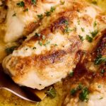 Juicy baked chicken thighs with golden crispy skin, garnished with fresh parsley, served in a flavorful yellow sauce in a baking dish.