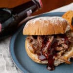 Juicy pulled pork sandwich with barbecue sauce on a blue plate, served with crispy tortilla chips, accompanied by an ice-cold bottle of Dr. Pepper soda, perfect for American comfort food meals.