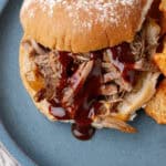Succulent pulled pork sandwich with barbecue sauce served on a bun, paired with crispy tortilla chips on a blue plate, perfect for a delicious meal.