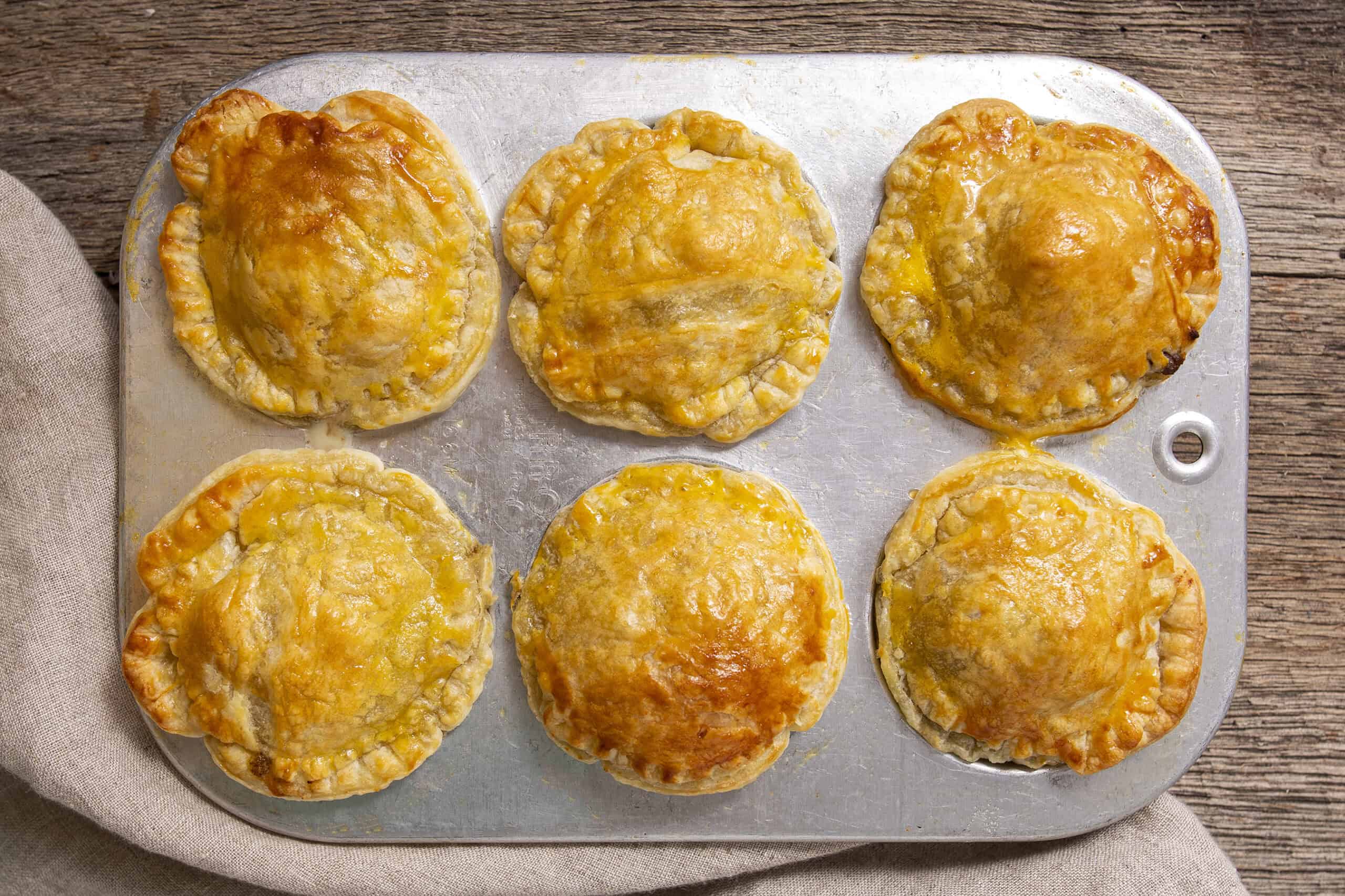 Golden baked chicken pot pies with flakey crusts on a baking sheet, perfect for savory comfort food recipes.