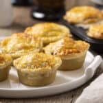 Golden baked cheese and chicken pot pies on a white platter, crispy crust, melted cheese topping, served on rustic wooden table.