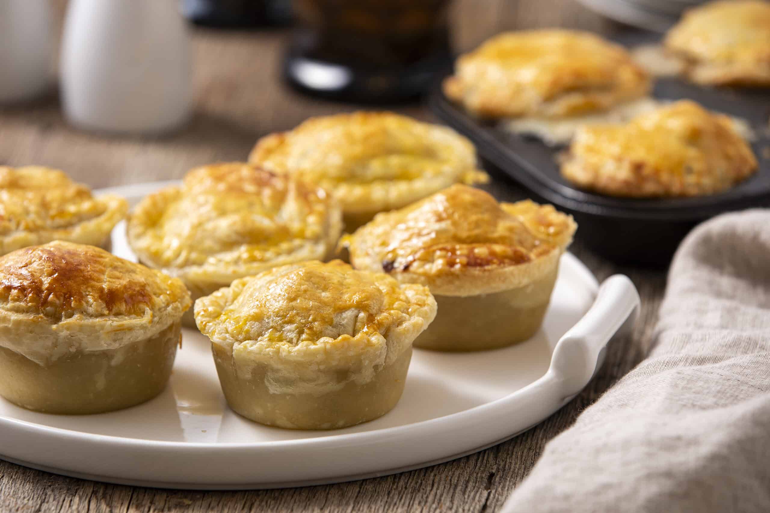 Golden baked cheese and chicken pot pies on a white platter, crispy crust, melted cheese topping, served on rustic wooden table.