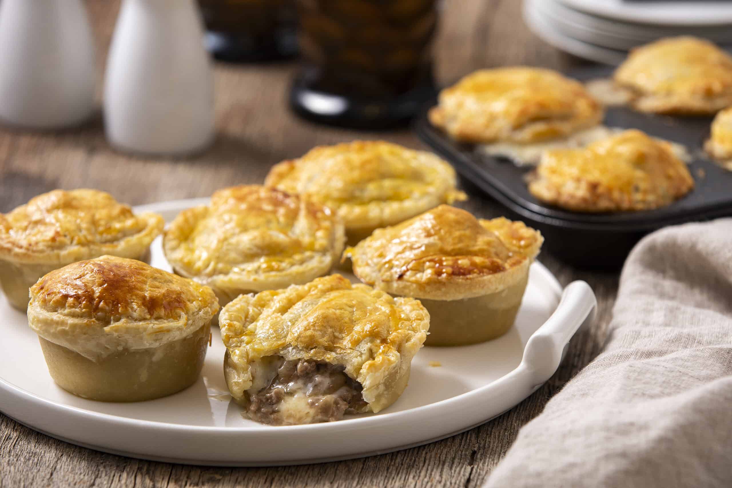 Savory mini beef pot pies with golden flaky crusts on a white ceramic platter, ideal for comfort food recipes and easy dinner ideas.