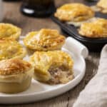 Golden baked savory pot pie muffins with flaky crust and hearty meat filling, served on a white plate. Perfect for comfort food or family dinner.