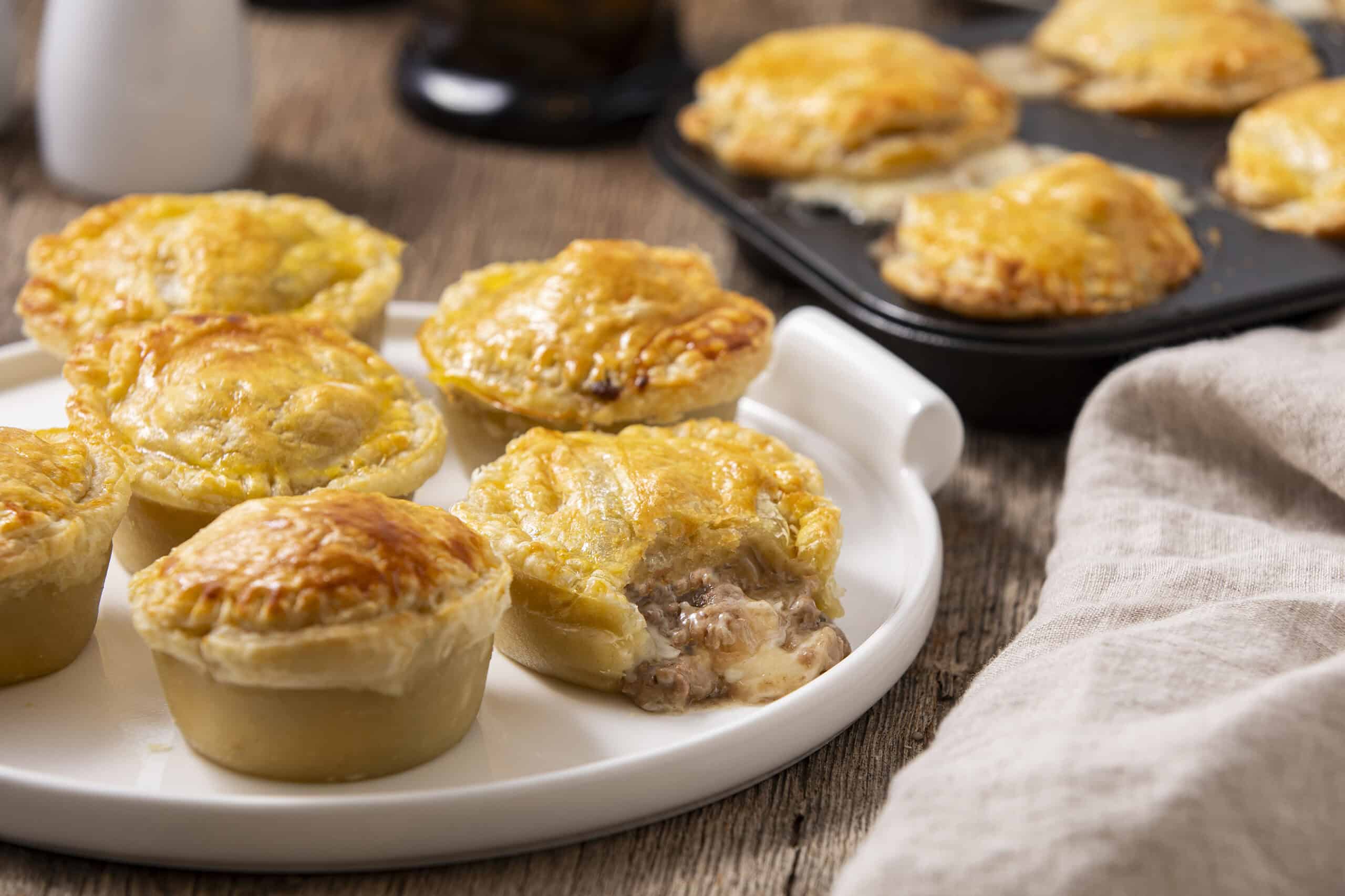 Golden baked savory pot pie muffins with flaky crust and hearty meat filling, served on a white plate. Perfect for comfort food or family dinner.