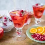 Refreshing pomegranate and orange citrus cocktail served in elegant glasses with fresh fruit garnishes, perfect for summer beverages or holiday parties.