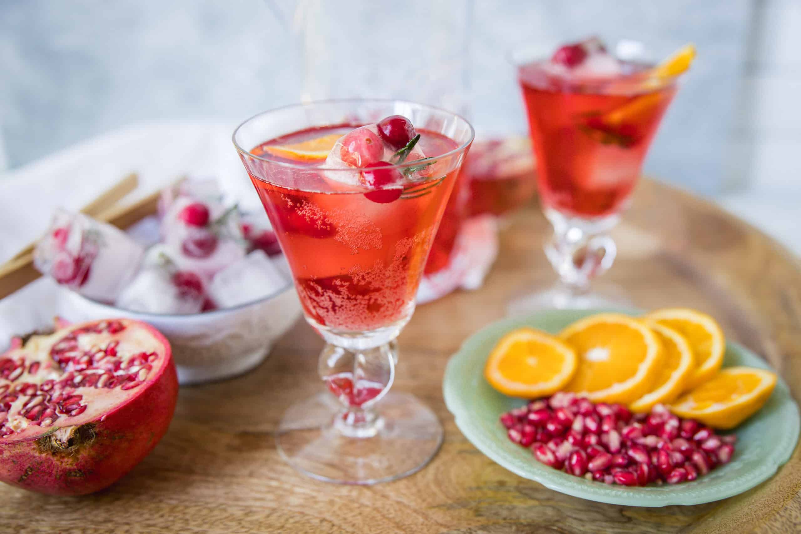 Refreshing pomegranate and orange citrus cocktail served in elegant glasses with fresh fruit garnishes, perfect for summer beverages or holiday parties.