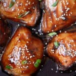Succulent sweet and savory glazed salmon fillets topped with sesame seeds and chopped green onions, cooked to perfection and served in a flavorful sauce.