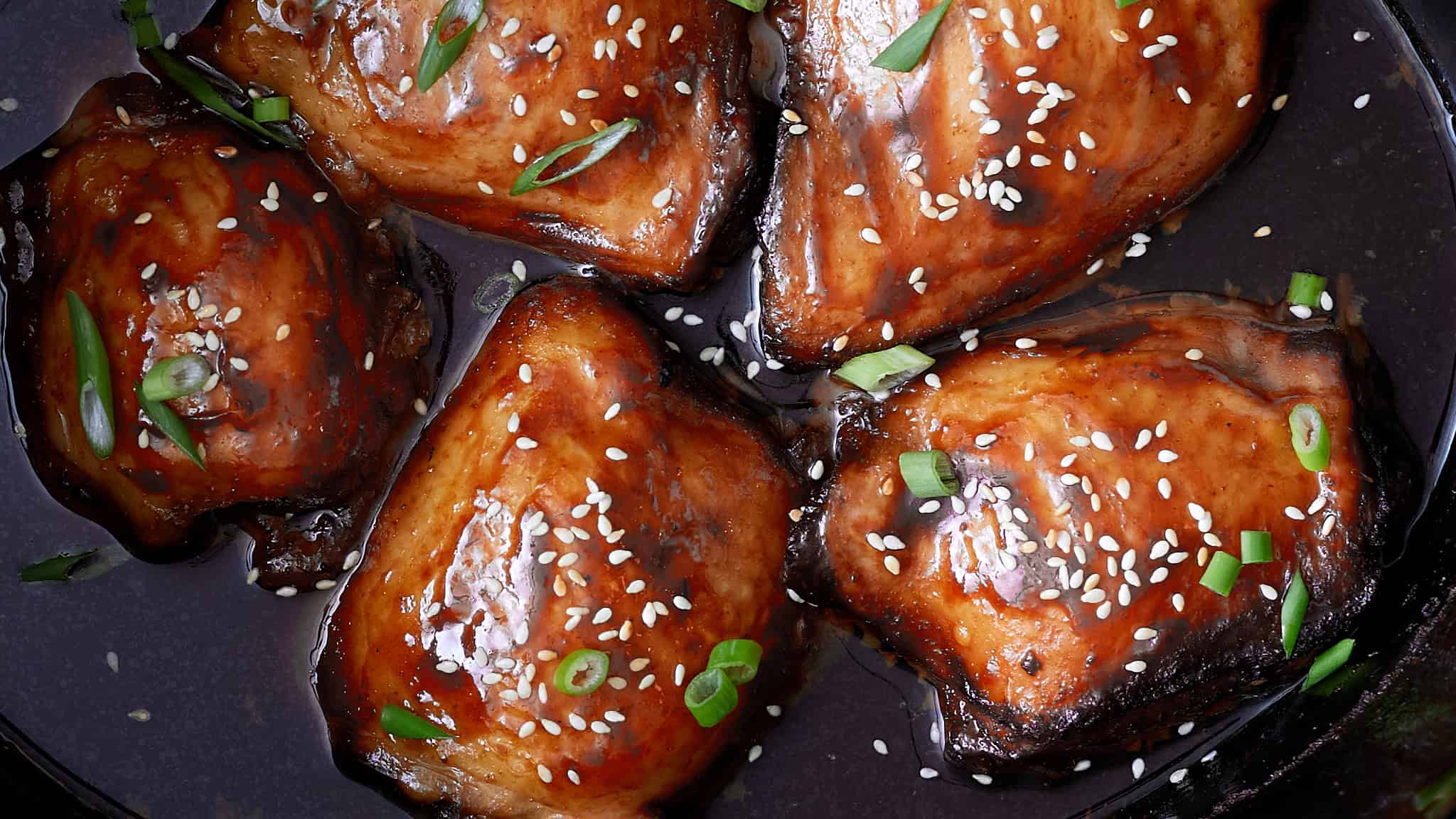 Succulent sweet and savory glazed salmon fillets topped with sesame seeds and chopped green onions, cooked to perfection and served in a flavorful sauce.