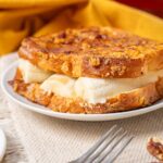 Golden baked banana bread pudding with creamy bananas on a white plate, served as a delicious dessert or snack on a textured beige tablecloth.