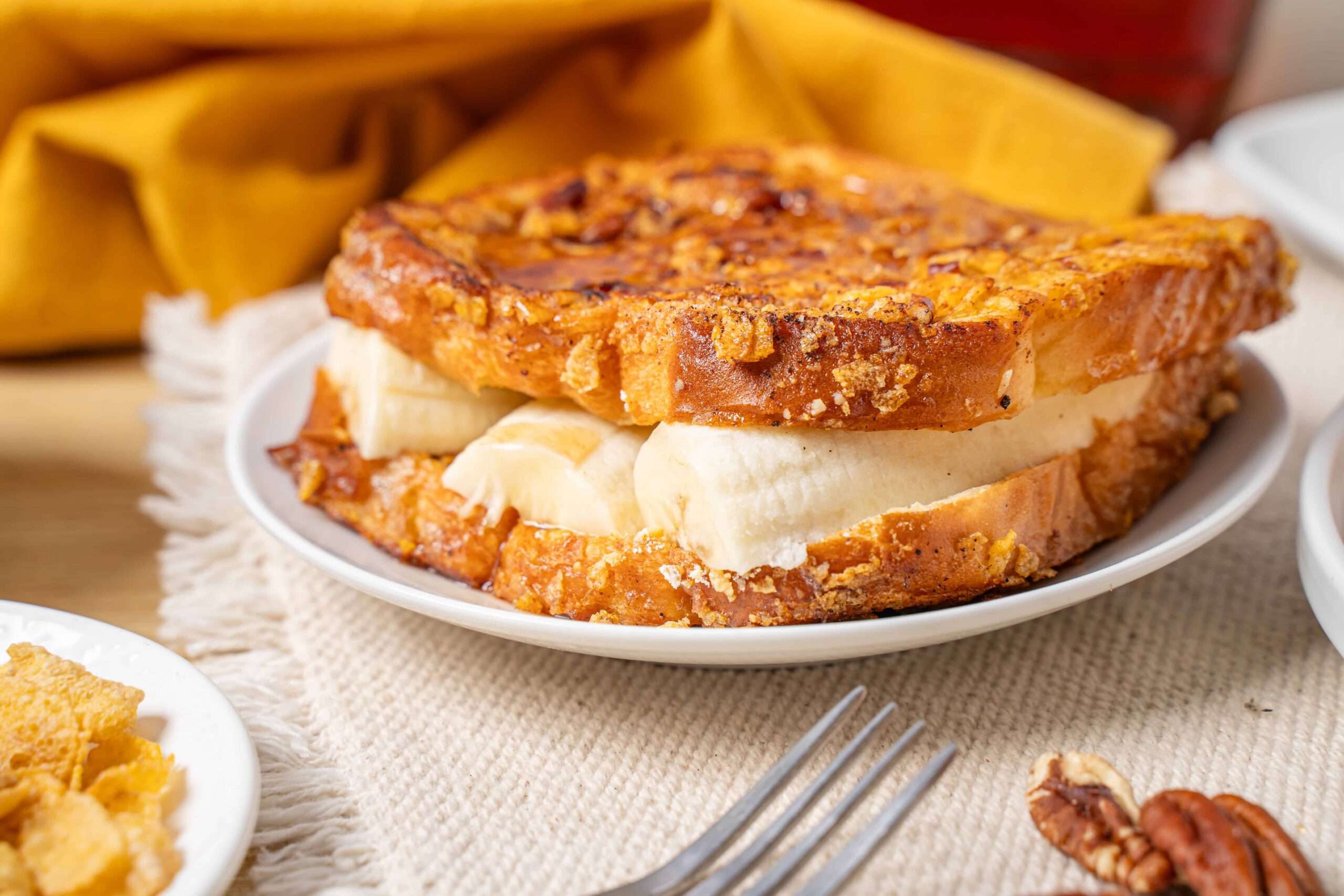 Golden baked banana bread pudding with creamy bananas on a white plate, served as a delicious dessert or snack on a textured beige tablecloth.