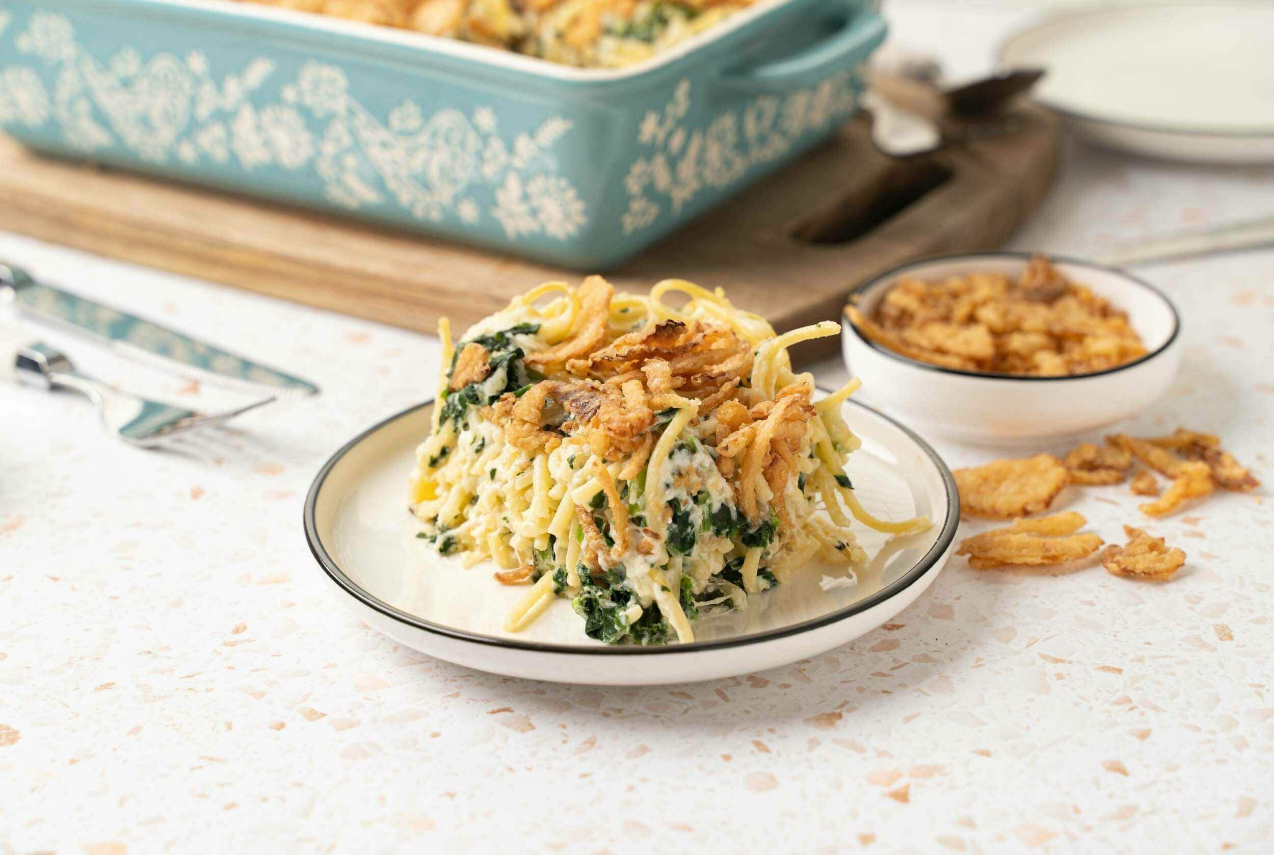 Crispy chicken and spinach casserole with shredded cheese and fried onions on a white plate, served with a side dish, baked in a turquoise baking dish, perfect for comforting family dinners and easy recipes.