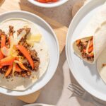 Savory beef taco with colorful vegetables on a soft flour tortilla, served on a white plate, ready for dinner or lunch.
