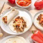 Savory beef taco filling with fresh vegetables on soft flour tortillas, ready to be rolled for delicious homemade tacos. Fresh peppers and ginger enhance the vibrant, flavorful presentation.